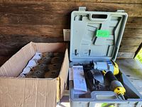Nailer in open gray plastic case with handle along with cardboard box of coil nails on wooden surface.