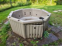 Full exterior view of octagonal beige hot tub on grass and pavers