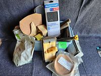 Wide shot showing plastic storage bin containing sandpaper rolls, sheets, wooden block tool, and other hand tools for sanding and scraping