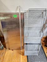 Two stainless steel counter tops of different sizes leaning against wall with a folding metal wire brochure rack on the right side. Measuring stick placed vertically for scale.