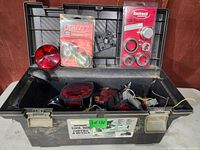 Open black plastic toolbox containing various trailer supplies including red trailer lights, packaged bearings, dust caps, plugs, and hardware parts.