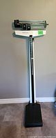 Full view of the upright mechanical medical scale with weight platform, vertical support, height ruler, and weighing mechanism.