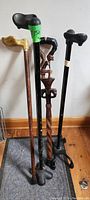 Four walking aids including three canes and a walking stick with rubber tips and varied handle styles.