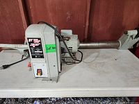 Full view of the lathe showing body, electrical motor, tool rest, and lathe bed on a white table.