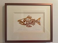 Full view of framed copper artwork depicting a salmon in Haida style, signed and titled, set against a wall.