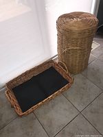 Wicker serving basket and tall wicker hamper side by side on tiled floor near window.