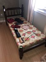 Full view of single wooden bed with floral patterned mattress and multiple small accessories placed on mattress.