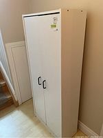 Front view of the white pressboard cabinet with two doors closed, flush against a wall near stairs.