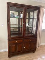 Front view of wood china cabinet showcasing two glass doors revealing glass shelves and mirrored back, two drawers, and lower storage doors.