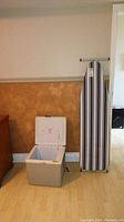 Photo showing Koolatron P27 electric cooler and striped ironing board standing upright beside it.