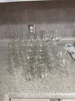 Multiple assorted glassware including champagne flutes, wine glasses, liquor glasses, and a small pitcher on a countertop.