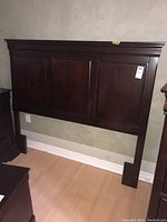 Full view of the dark stained wooden headboard against the wall, showing its height and length.