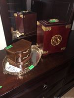 Smaller wooden two-drawer jewelry box and silver-tone decorative vanity tray on wooden surface with reflection