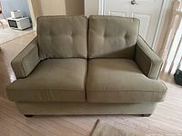 Front view of beige/olive upholstered love seat with two seat cushions and two back cushions with button tufting.