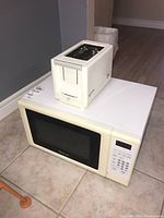 White microwave oven with black window and digital keypad. White two-slice toaster on top.
