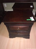 Front view of wooden nightstand with two drawers and metal ring handles, showing overall shape and color.