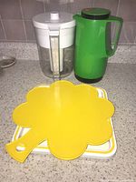 Clear Brita water pitcher, green insulated pitcher, yellow clover-shaped serving tray, white rectangular serving tray on kitchen counter.