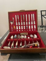 Full view of cutlery set inside an open wood box with red felt interior, showing knives, forks, spoons, and other utensils.