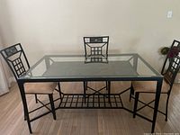 Full front view of metal and glass dining table with three chairs around it.