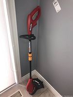Full view of the red and black Homelite electric string trimmer standing upright in corner showing handle and shaft.