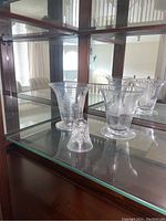 Photo showing two etched glass vases and one crystal bell on a glass shelf with mirrored background.