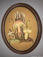 Front view of oval wooden framed embroidered mushroom art on textured fabric background