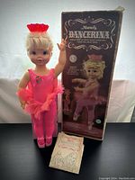 Full view of the 1969 Mattel Dancerina doll standing next to its original box and instruction booklet on a black surface.