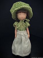 Full body photo of 1974 Holly Hobby Amy doll in green gingham dress with puff sleeves, cream polka dot apron, and matching bonnet.