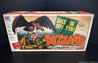 Board game box featuring illustration of a large buzzard attacking a character near a pyramid, with branding and game info.