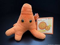 Front view of the orange Amoeba Giant Microbes plush toy with black eyes, approx. 5 inches tall, including attached tags and informational card.