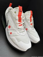 Side and angled view of both shoes showing overall design including white mesh and synthetic upper, bright orange pull tabs and black Nike swoosh logo, white midsole with visible air unit, and black outsole.