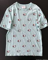 Light blue Champion men's t-shirt with repeated large Champion 'C' logos printed all over the fabric, laid flat to show front, highlighting design and condition.