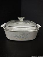 Front view of the rectangular CorningWare casserole dish with the Country Cornflower pattern and clear Pyrex glass lid on top against a black background.
