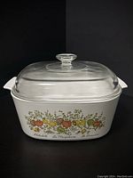 Front view of white Corning Ware casserole dish with colorful Spice of Life pattern and clear Pyrex lid on top.