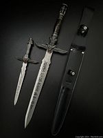 Full view of both Egyptian style daggers and black leather scabbard lying on dark surface.