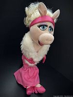 Miss Piggy plush doll in pink dress with white fur collar shown standing against black background.