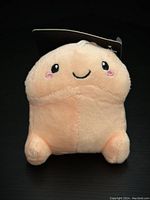 Front view of beige adult novelty plush with smiling face and four rounded feet, tag attached at back
