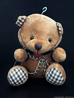 Front view of the brown teddy bear plush with checkered ears and feet, chains, and straps.