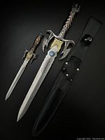 Photo of two stainless steel decorative daggers with embellished handles and a black sheath on a black surface.