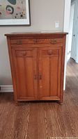 Front view of antique wooden cabinet showing single drawer and double doors with handles and keyholes.
