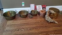 Full view of all brass pots, copper mold, parchment paper boxes, and baking cups arranged on floor.