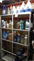 Full view of shelving unit with assorted cleaning products arrayed on four shelves including large bleach bottles, sprays and liquid cleaners in different sized containers.