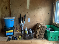 Shelf with blue bucket on black ROOFMELT container, hand pruners, large grass clippers, brown folded garden bags, green basket with gloves and other items