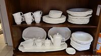 Overall view of all dishes on shelving including plates, cups, serving platter, tray, gravy boat, coffee pot, and sugar bowl