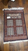 Full view of vintage small area rug with fringe on wooden floor. Shows overall geometric and rectangular pattern and colors.