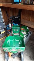 Green Scotts Turf Builder EdgeGuard push spreader in a wooden shed with gardening supplies behind it.