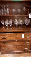 Full view of the collection on wooden shelves showing champagne coupes on top shelf, assorted glasses and wine glasses on lower shelves.