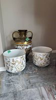 Overview of urn and two pots showing gold and brown decorative motifs with handles on urn and bird/floral designs on pots.