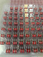 Close-up photo showing multiple red and silver TDK surge arresters with two metal leads arranged in plastic tray.