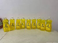 Nine clear plastic bottles of lemon-scented Great Value dish soap lined up on a table.